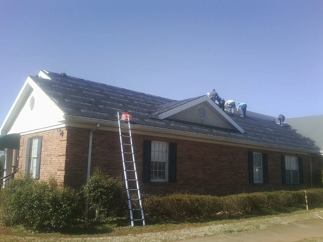 Crew tearing shingles off a brick ranch roof with a ladder set — Emergency Roof Repair work by our crew in Rosalia