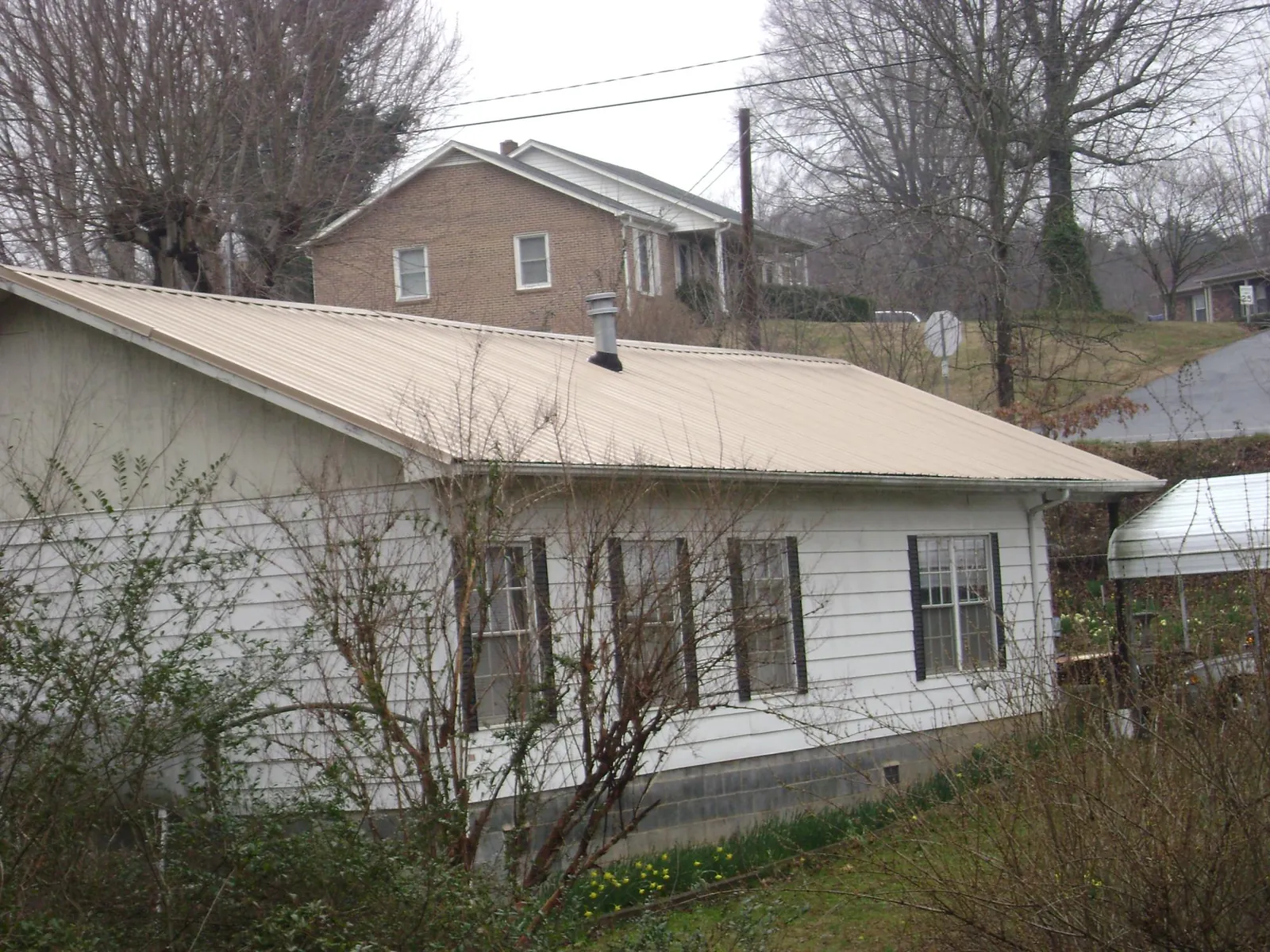 Tan metal roof on a white sided house set into a hillside — Commercial Roofing by Roofing Brothers in Rosalia